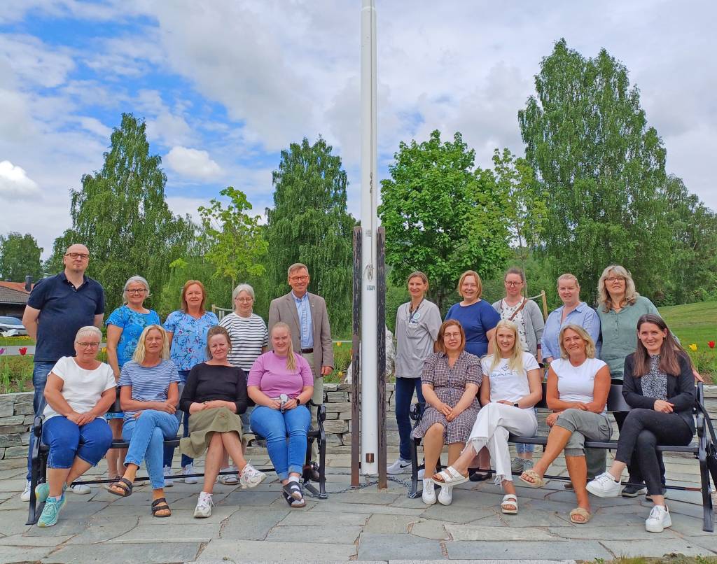 18 mennesker oppstilt ved en flaggstang, både kvinner og menn