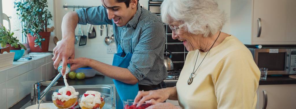 Eldre dame og ung mann står på et kjøkken og lager dessert